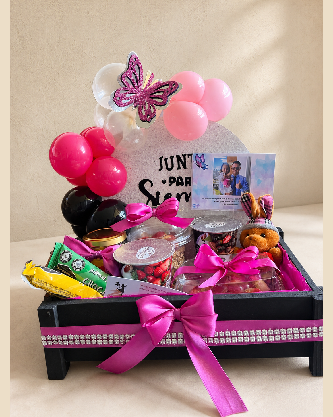 Ancheta de regalo con globos rosas y negros, dulces y cartel personalizado