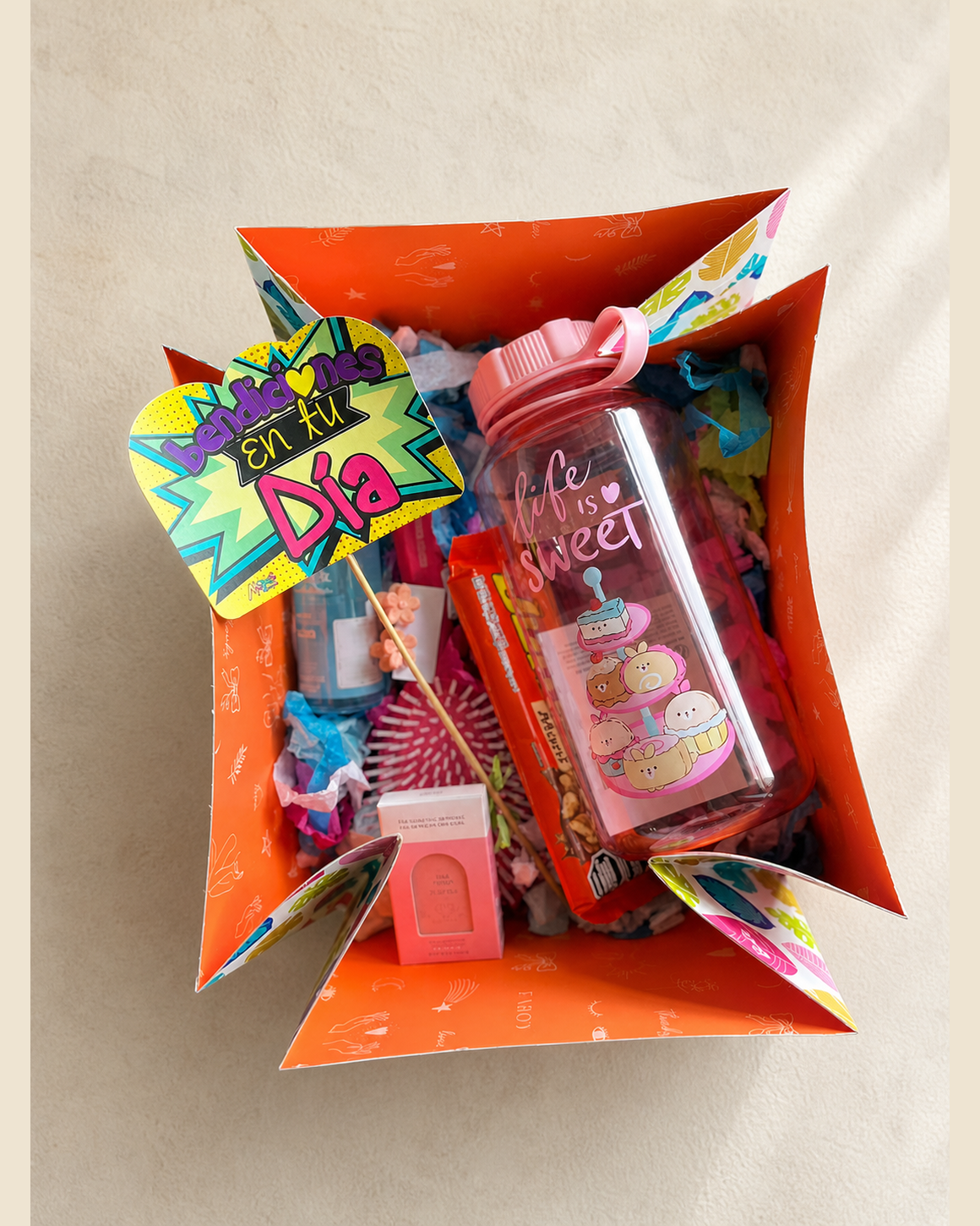 Caja de regalo abierta en naranja con cartel bendiciones en tu día, botella térmica, snacks y detalles de cuidado personal