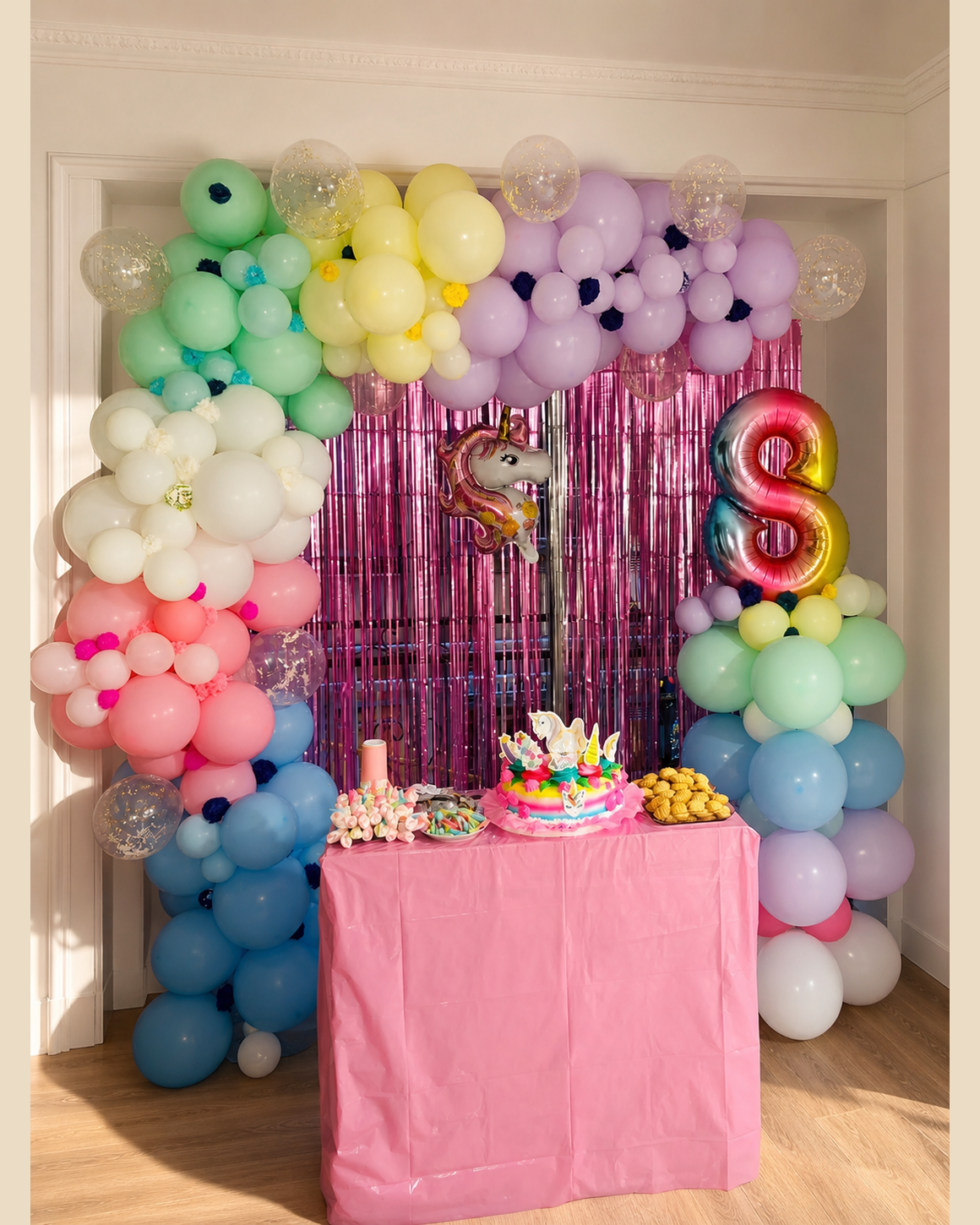 Decoración infantil con globos pastel, cortina de flecos rosa y mesa de tarta