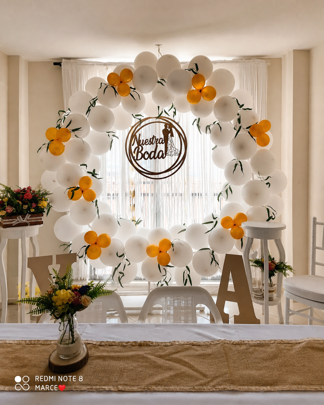 Aro de globos blancos y dorados con cartel de nuestra boda y flores