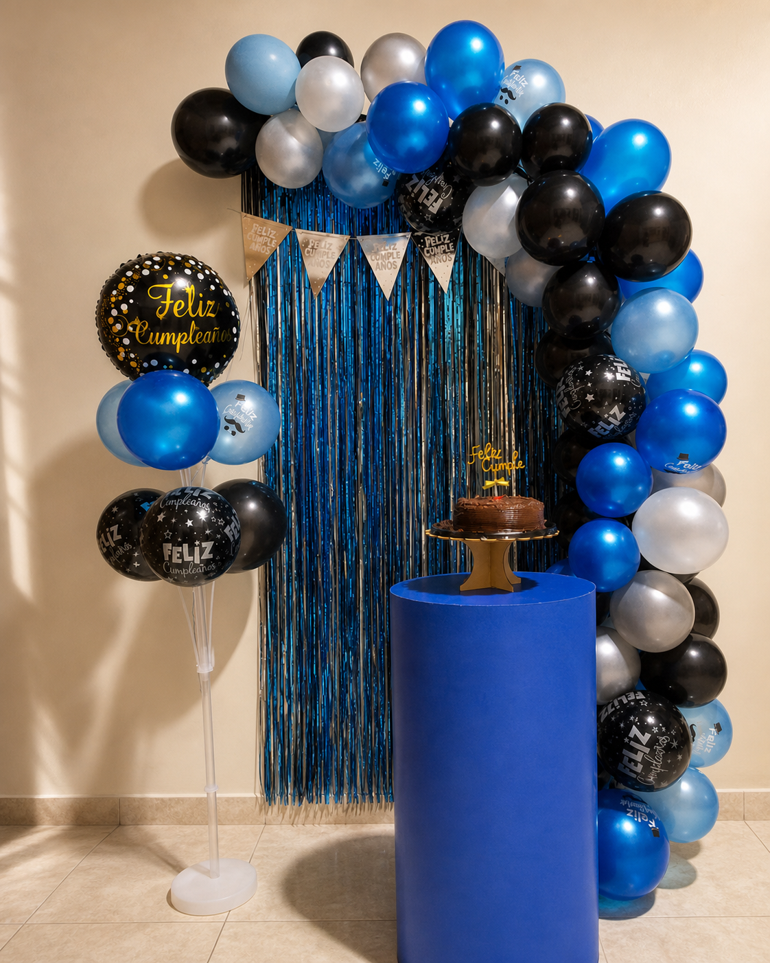 Composición de globos en azul, negro y plata con cortina de flecos y columna para la tarta