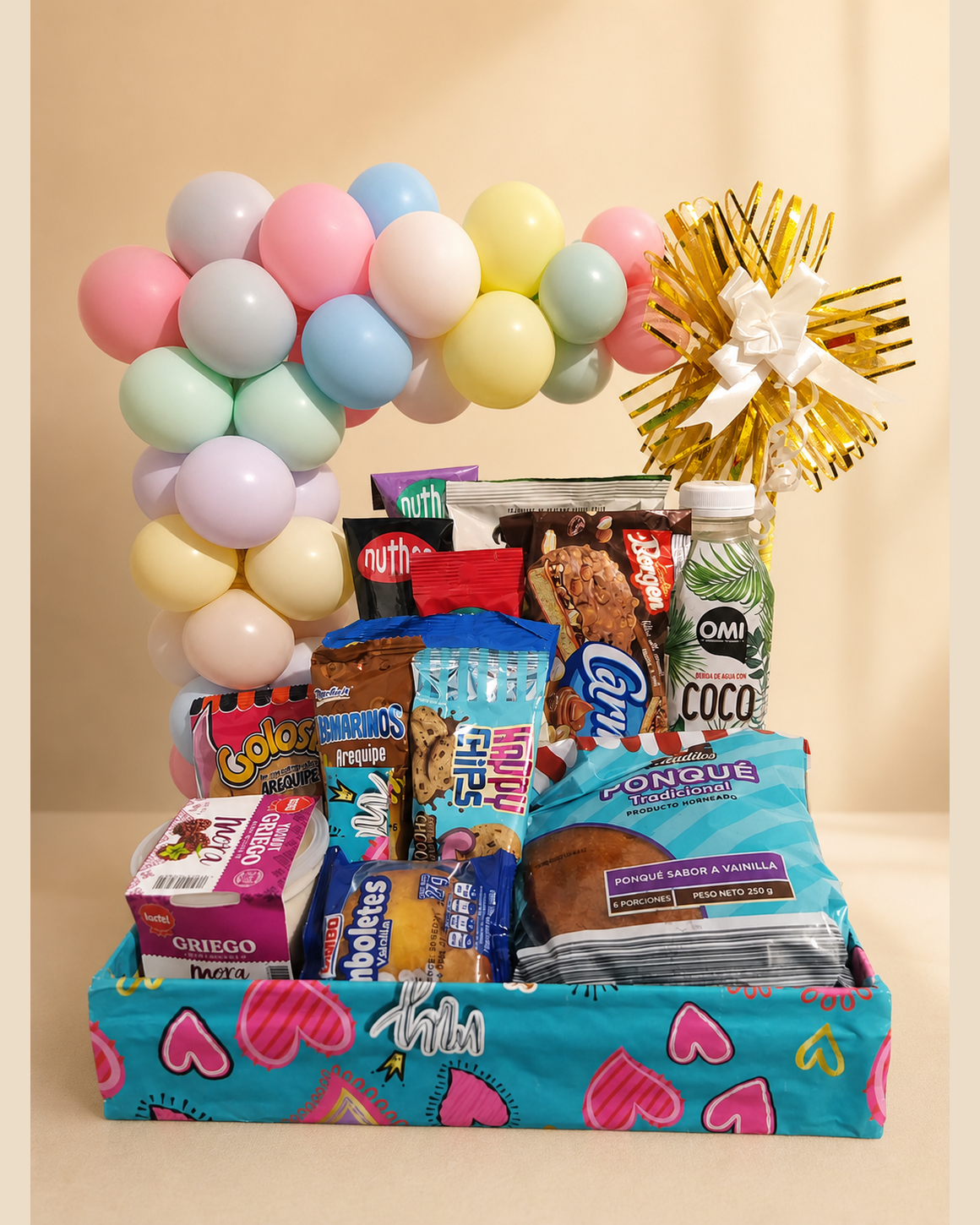 Ancheta con globos pastel, dulces y snacks sobre caja estampada